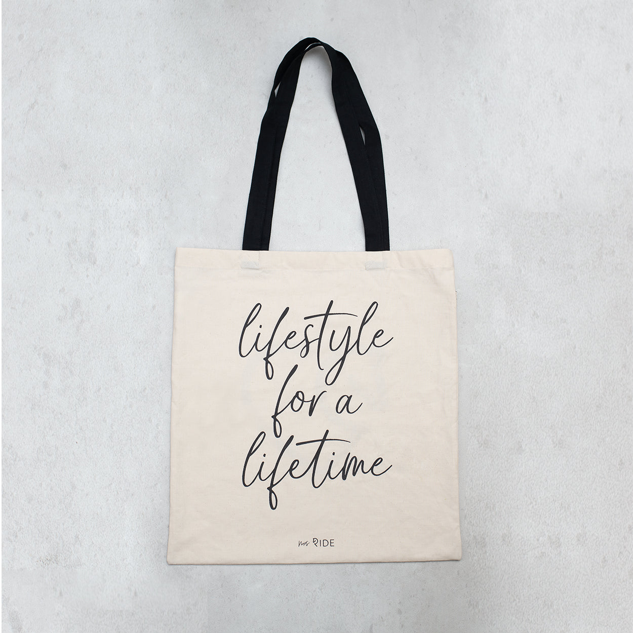 Helle Baumwolltasche mit schwarzer schrift auf grauem Untergrund 