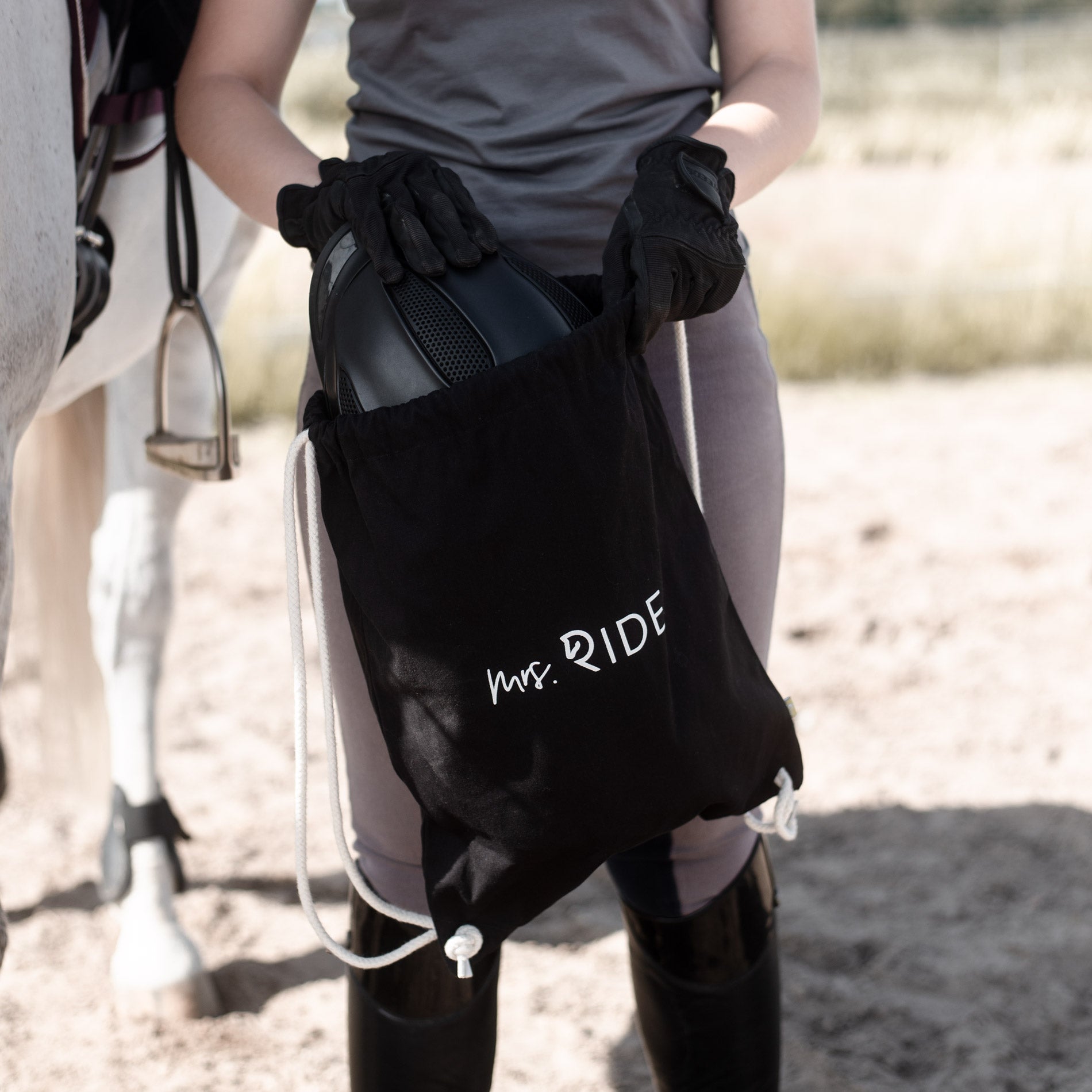 Frau steck einen Reithelm in einen schwarzen Rucksack